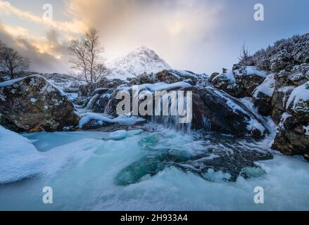 Der gefrorene Fluss Coupall fließt an einem winterlichen Tag in Glencoe, Schottland, an Stob Dearg (dem markanten Gipfel auf Buachaille Etive More) vorbei. Stockfoto