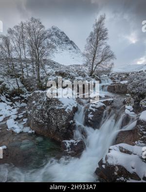 Der gefrorene Fluss Coupall fließt an einem winterlichen Tag in Glencoe, Schottland, an Stob Dearg (dem markanten Gipfel auf Buachaille Etive More) vorbei. Stockfoto