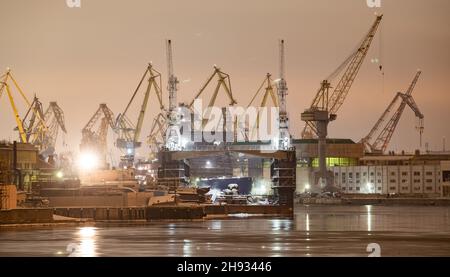 Der Bau von nuklearen Eisbrechern in der Nacht, Kräne der baltischen Werft in einem frostigen Wintertag, Dampf über dem Fluss Neva, glatte Oberfläche Stockfoto