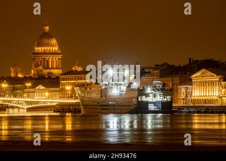 Die Panoramabilder der Winternachtstadt Sankt-Petersburg mit malerischen Spiegelungen auf dem Wasser, großes Schiff, das in der Nähe der Blagoweschtschenski Brücke oder festgemacht ist Stockfoto