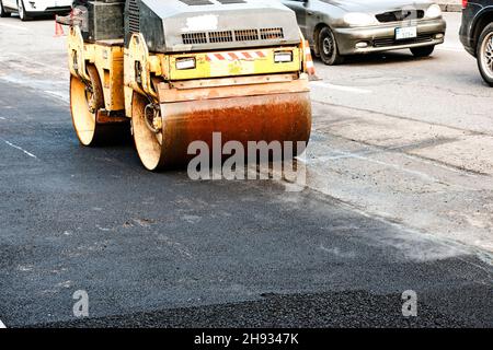 Kompakte Dampfwalze glätten den Asphalt. Schwere Vibrationswalze auf Asphalt arbeitet. Fragment des Rollenrads, städtische Straße ist im Aufbau Stockfoto