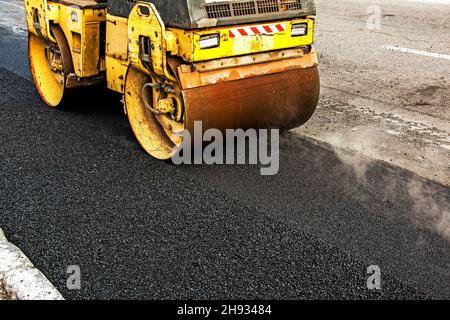 Kompakte Dampfwalze glätten den Asphalt. Schwere Vibrationswalze auf Asphalt arbeitet. Fragment des Rollenrads, städtische Straße ist im Aufbau Stockfoto