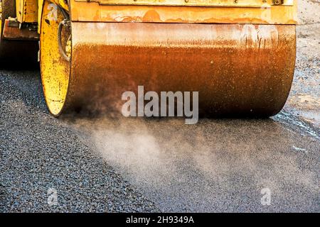 Kompakte Dampfwalze glätten den Asphalt. Schwere Vibrationswalze auf Asphalt arbeitet. Fragment des Rollenrads, städtische Straße ist im Aufbau Stockfoto