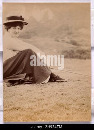 Vintage-Foto von Young Woman saß auf Gras lächelnd, trägt Strohhut, Englisch, anonym, 1910s Stockfoto