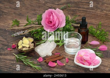 Romantische Liebestrank-Kräuter und Rosenblüten in einem Hexenbündel mit Quellwasser, Tinktur-Flasche, Zimt und Ingwer-Gewürz mit Quarzkristall gebunden Stockfoto