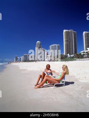 Australien. Queensland. Surfers Paradise. Zwei junge Frauen sitzen auf Stühlen am Strand. Stockfoto