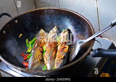 Drei Karauschen werden in einem Wok mit grünen und roten Chilischoten in der Küche einer chinesischen Familie gebraten. Stockfoto