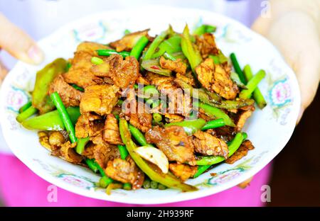 Chinesisches hausgemachtes Gericht doppelt gekochter Schweinebauch mit grünen Chilischoten auf einem Teller. Stockfoto