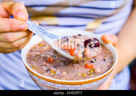 Frau Hände Löffel Multi-Korn-Brei aus einer Schüssel mit Jujube und Goji-Beere auf. Stockfoto