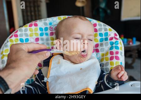 Ein kleines Mädchen (ca. 10 Monate alt) wird Löffel gefüttert ihr Abendessen der pürierte Nahrung und lehnt einen Löffel mit einem angewidert Gesicht. Stockfoto