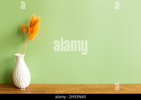 Vase von orangen Hasen Schwanz Gras trockene Blumen auf Holztisch. Grüne Wand Hintergrund. Kopieren Raum Stockfoto