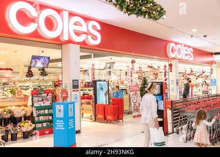 Mutter trägt Gesichtsmask mit Kleinkind, das während einer Coronavirus-Pandemie in Sydney in den Coles Supermarkt zum Einkaufen eindringt. Dezember 2021 Stockfoto