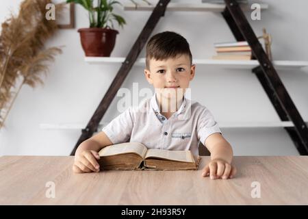 Portrait eines jungen Studenten, der an einem Schreibtisch sitzt und online studiert und dem Lehrer zuhört. Schuljunge macht Hausaufgaben sitzen mit einem offenen Lehrbuch oder Buch Stockfoto