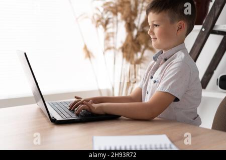 Seitenansicht eines Schuljungen zu Hause, der an einem Laptop arbeitete und Text auf der Tastatur tippte, während er mit einem Lehrer aus der Ferne kommunizierte. Das Kind ist es Stockfoto