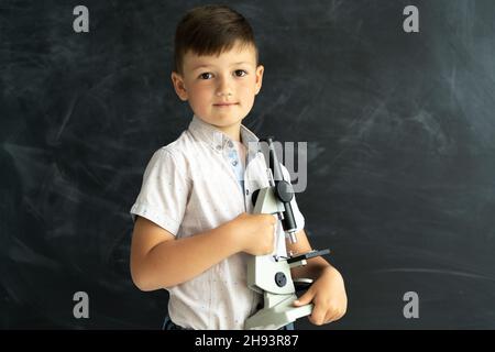 Biologieunterricht in der Schule. Schuljunge mit einem Mikroskop in der Nähe des Kreidetafels im Klassenzimmer. Fokussiertes Lernen Für Schüler. Nahaufnahme eines Studenten bei Stockfoto