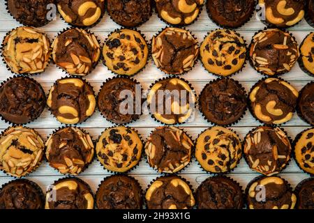 Blick von oben auf frische hausgemachte leckere Vanila und Schokolade Muffins in Papier Cupcake Halter isoliert auf Holzhintergrund. Stockfoto