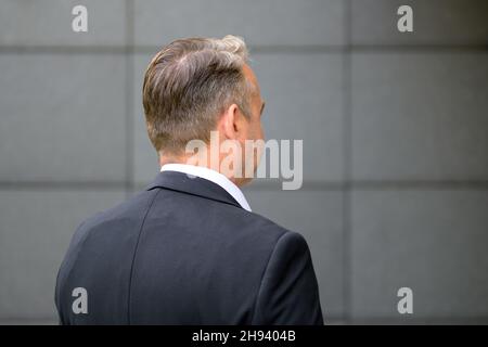 Rückansicht Porträt eines selbstbewussten, gutaussehenden Mannes mittleren Alters, der ein elegantes weißes Hemd und eine Jacke an der grauen Wand trägt, um Platz für Kopien zu schaffen Stockfoto