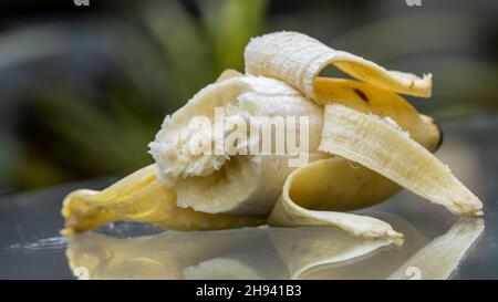Halb gefressene Banane mit Schatten auf dem Glas, offene Banane isoliert auf einem Außenhintergrund. Stockfoto