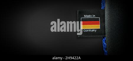 Etikett mit deutscher Flagge und Text made in Germany, auf schwarzem Stoff genäht, auf schwarzem Hintergrund mit Kopierfläche. Stockfoto