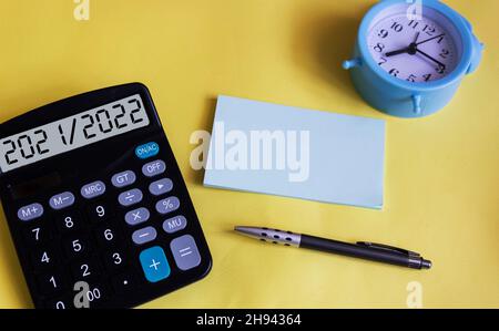 Der Text 2021 2022 auf dem Display eines Rechners. Auf gelbem Hintergrund eine Uhr, ein Stift und ein Notizbuch zum Schreiben. Planung für das neue Jahr Stockfoto