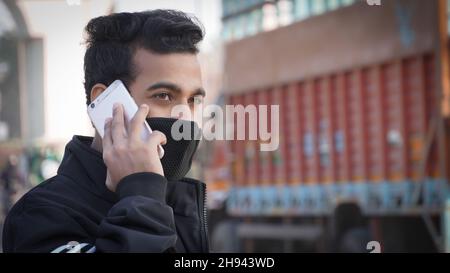 Junger Mann, der das Mobiltelefon hält, das Smartphone benutzt, einen Anruf macht, am Telefon spricht, auf der Straße steht und den Verkehrsverkehr im Hintergrund hat Stockfoto