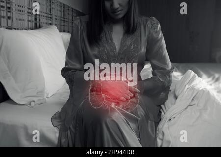 Asiatische Frau in Satin-Schlafkleidung mit Magenschmerzen in der Nacht. Stockfoto