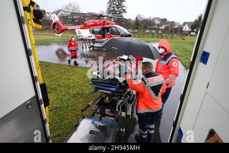 02. Dezember 2021, Baden-Württemberg, Öhringen: Während einer Mission hält ein Sanitäter einen Regenschirm über einem Patienten, der von einem Krankenwagen zum DRF-Rettungshubschrauber Christoph 51 zum weiteren Transport gebracht wird. Während der Mission transportierte der DRF einen Patienten ohne Covid-19 im DRF-Rettungshubschrauber Christoph 51 von der Intensivstation des Krankenhauses Hohenlohe auf die Intensivstation einer Reha-Klinik in Bayern. Covid 19 Patienten sind nicht die einzigen, die jetzt per Hubschrauber von einem Krankenhaus zum anderen transportiert werden. Um Kapazität in zu schaffen Stockfoto