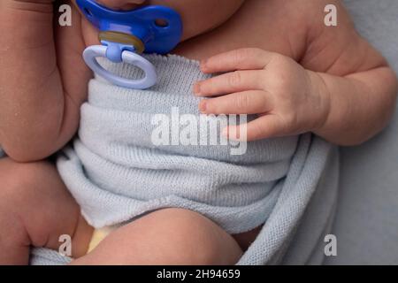 Ein neugeborenes Baby in einer blauen Wicklung schläft auf einem blauen Hintergrund. Hand und Finger des Neugeborenen. Schnuller aus nächster Nähe. Studio macrophoto. Stockfoto