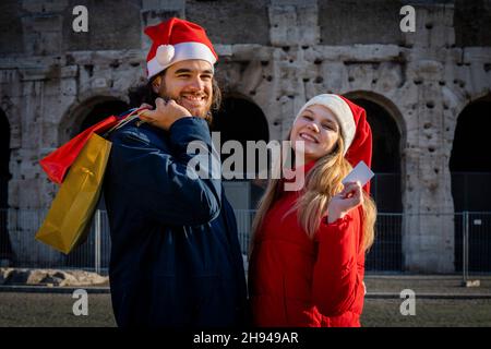 Weihnachtseinkäufe. Das lächelnde junge Paar hat gerade Weihnachtsgeschenke gekauft. Er bringt die Umschläge mit Geschenken und sie zeigt ihre Kreditkarte Stockfoto