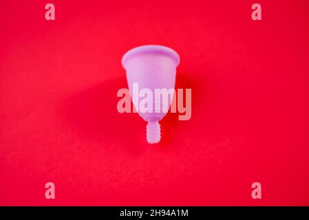 Eine Menstruationsbecher aus Silikon auf rotem Hintergrund isoliert. Stockfoto