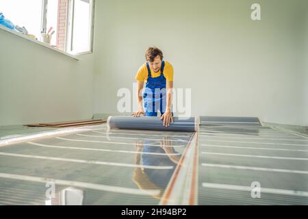 Master installiert einen warmen Fußboden im Raum. Installation der Fußbodenheizung Stockfoto