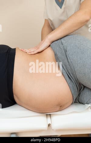 Physiotherapeutin, die eine auf der Seite einer Schwangeren auf einem Massageliegen in einem Gesundheitszentrum liegende Frau massiert Stockfoto