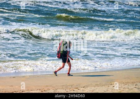 Baltiysk, Russland - 07.30.2021 - Junge Backpacker-Frau, die auf dem Meer unterwegs ist. Mädchen Reisende mit großen roten Rucksack erkunden neue Region, schöne Balt Stockfoto