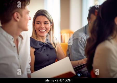 Eine junge Frau genießt eine Gesellschaft ihrer Kollegen während eines Geschäftsvortrags in entspannter Atmosphäre im Konferenzraum. Unternehmen, Menschen, Treffen Stockfoto