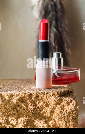 Roter Lippenstift und Parfüm auf einem Naturstein-Laufsteg. Stockfoto