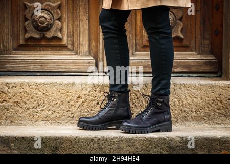 Trendige schwarze Stiefel. Modische Lederschuhe aus nächster Nähe. Weibliche Beine stehen auf der Treppe auf der Straße Stockfoto