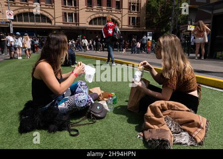 Melbourne, Australien, 4. Dezember 2021. Zwei Frauen genießen das Mittagessen in der Sonne auf der Elizabeth Street, während der Protestierende während des letzten „aufhebungsmarsches“ von Tausenden Demonstranten vom parlamentsgebäude zur Flinders Street Station marschiert, um die Kreuzung zu halten. Demonstranten marschierten in den Büros des ABC- und Regierungshauses. Quelle: Michael Currie/Speed Media/Alamy Live News Stockfoto