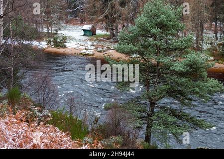 RIVER SPEY SCHOTTLAND WINTERSCHNEESZENE EINE ALTE GRÜNE FISCHERHÜTTE AM FLUSSUFER Stockfoto