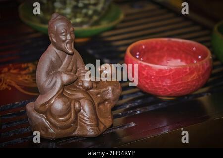 Fragment der Teezeremonie mit Keramikfigur des Salbei des Tees Lu Yue im Vordergrund, chinesische klassische Teekultur. Stockfoto