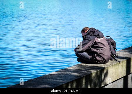 HAMBURG, DEUTSCHLAND - 10. Mai 2017: Ein Mann sitzt an der Wand am Rande eines Sees in Hamburg, Deutschland Stockfoto