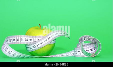 Grüner Apfel mit grauem Maßband auf grünem Hintergrund in gesunder Ernährung und Diät-Konzept Stockfoto
