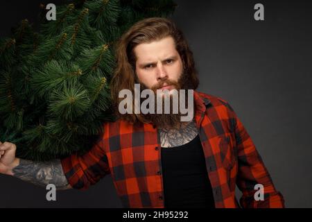 Schöner Mann mit langen Haaren, der einen synthetischen weihnachtsbaum hält. Stockfoto