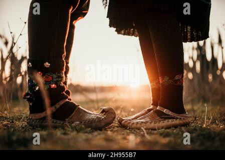 Paar in traditionellen serbischen Kostümen und Schuhen auf einer Wiese bei Sonnenuntergang Stockfoto