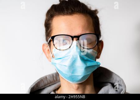 Junger Mann mit nebligen Gläsern durch das Tragen von Einwegmaske verursacht. Schutzmaßnahme während einer Coronavirus-Pandemie Stockfoto