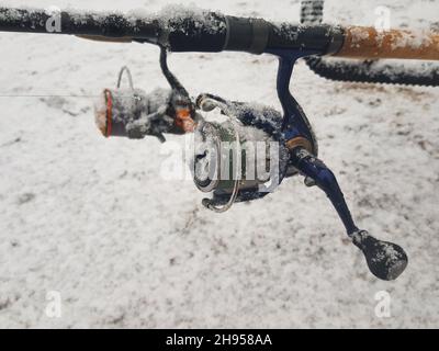 Angeln auf dem Futterhäuschen, im Fluss. Angelrute und Walze aus der Nähe. Die Angelausrüstung war mit Schnee bedeckt. Stockfoto