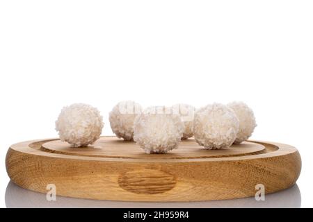 Mehrere runde Süßigkeiten mit Kokosflocken auf einem Holztablett, Nahaufnahme, isoliert auf Weiß. Stockfoto