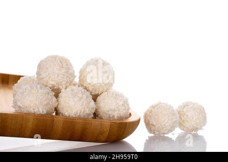 Mehrere runde Süßigkeiten mit Kokosflocken auf einem Holztablett, Nahaufnahme, isoliert auf Weiß. Stockfoto