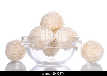 Mehrere runde Süßigkeiten mit Kokosflocken in einer Glasschale, Nahaufnahme, isoliert auf Weiß. Stockfoto