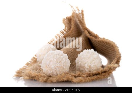 Mehrere runde Süßigkeiten mit Kokosflocken auf einer Jute-Serviette, Nahaufnahme, isoliert auf Weiß. Stockfoto