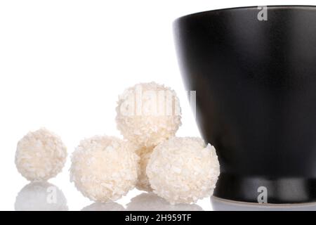 Mehrere runde weiße Bonbons mit Kokosflocken mit einer Keramikschale, Nahaufnahme, isoliert auf Weiß. Stockfoto